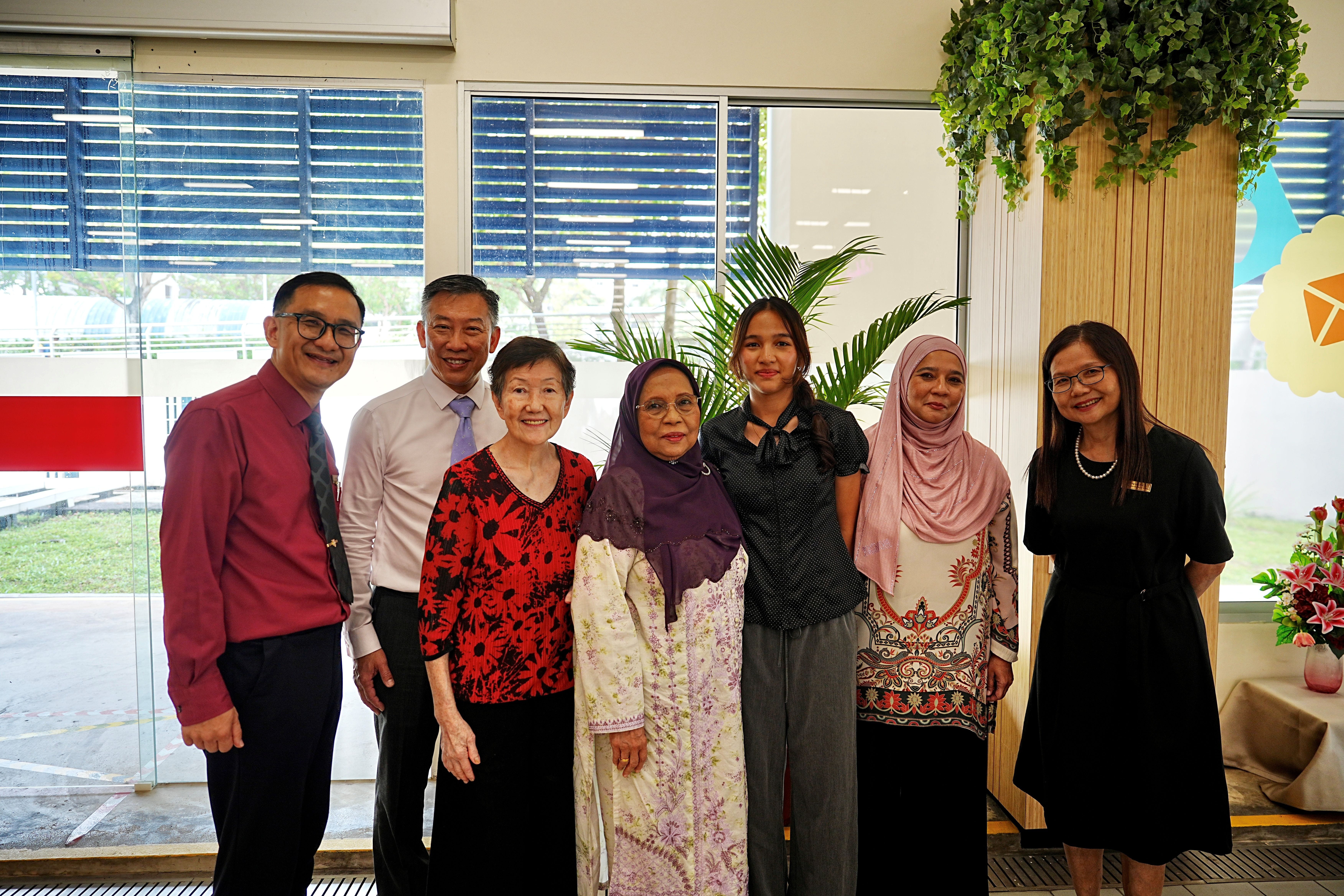 The valedictorian posing with family members and school staff in a bright foyer after the College Day ceremony.